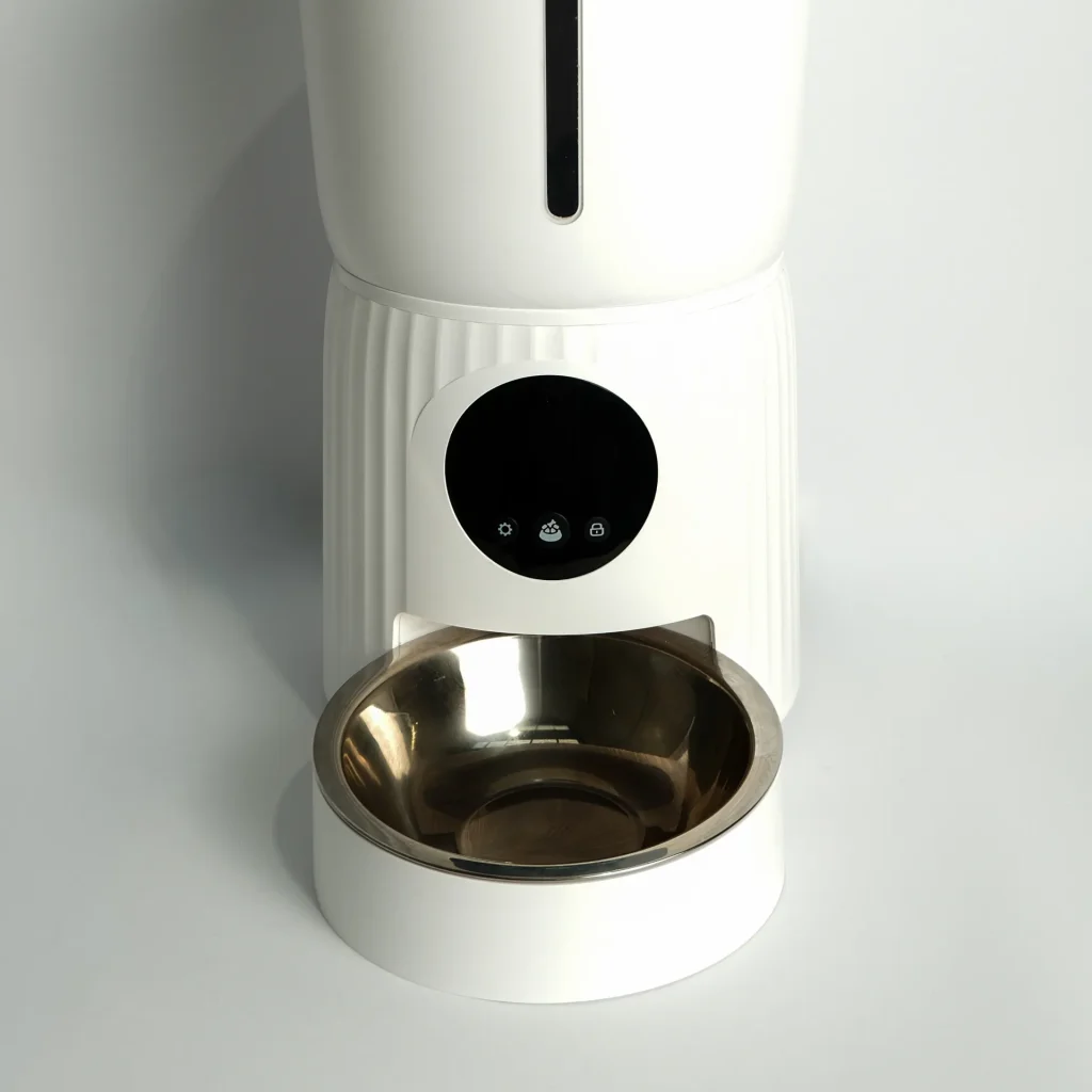 Close-up of the white automatic pet feeder dispensing a controlled portion of kibble into the bowl.